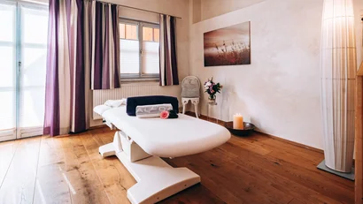 Heller Massageraum mit Behandlungsliege, Kerze und Blumendekor