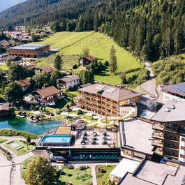 Luftaufnahme eines Hotels mit Pool, Rutsche und Fitnessbereich in grüner Berglandschaft