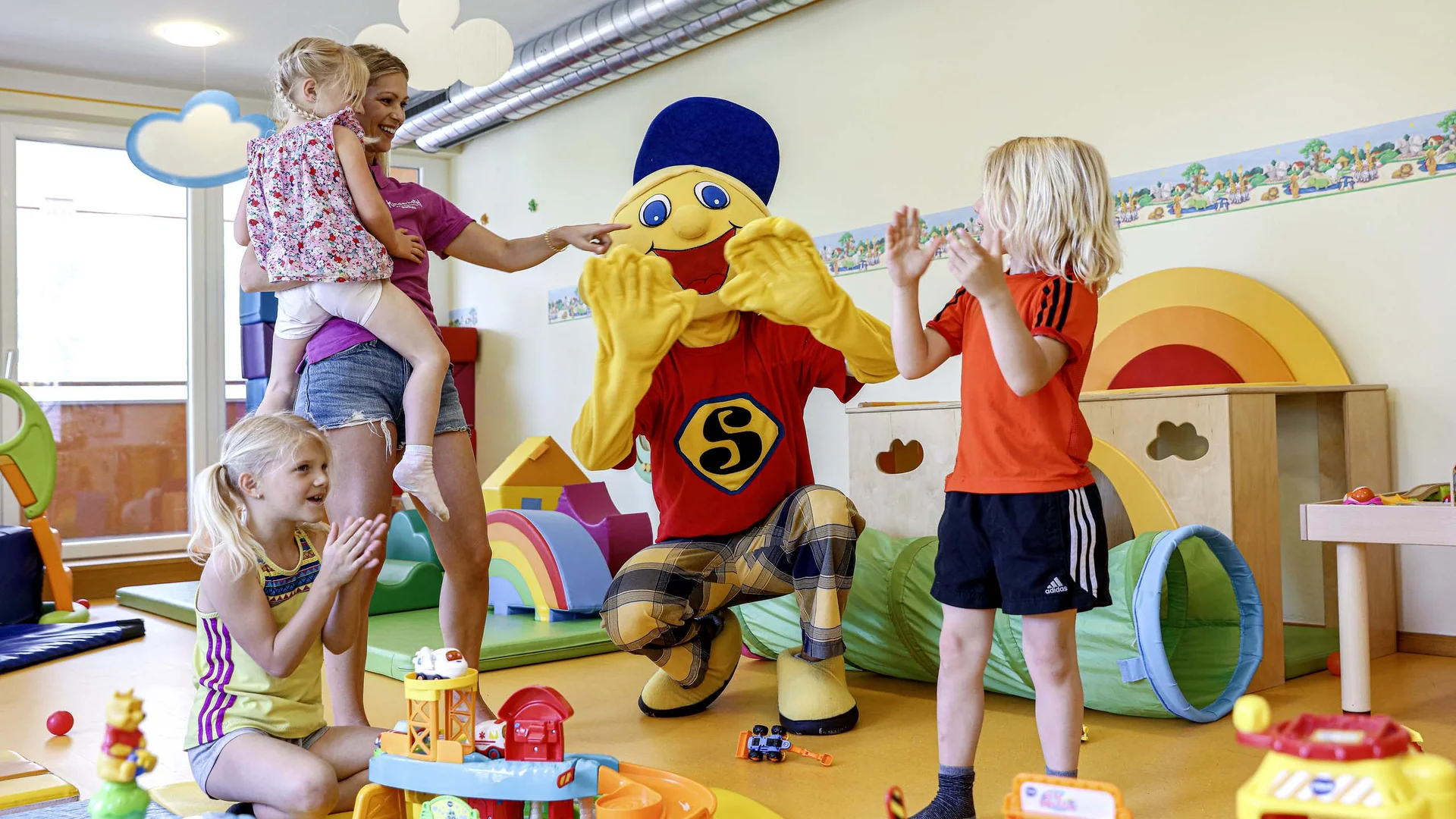 Kinder spielen mit einer Person in Kostüm in einem bunten Spielzimmer