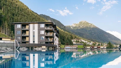 Hotel mit Außenpool vor bewaldeten Bergen und blauem Himmel