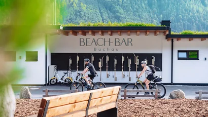 Zwei Radfahrer an der Beach Bar Buchau mit grünen Bergen im Hintergrund